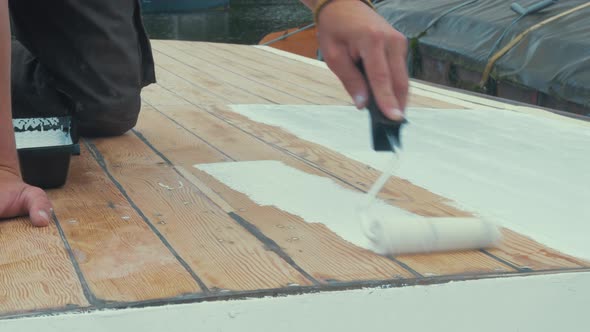 Applying thinned coat white primer on wooden boat roof with roller