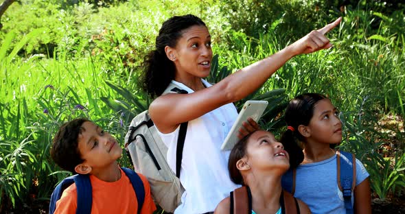 Woman interacting with kids while using digital tablet in park