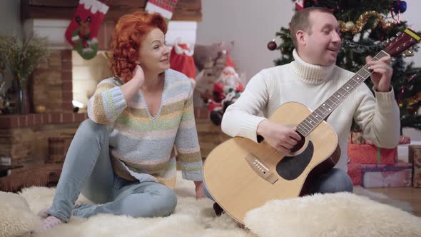 Wide Shot Portrait of Happy Relaxed Caucasian Man and Woman Playing Guitar and Singing on Christmas