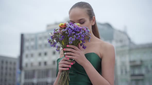 Beautiful Girl in Chic Dress Standing with Fragrant Bouquet of Wildflowers on the Background of the