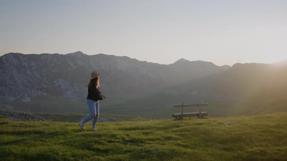 Happy travel woman in hat  spins around against mountain landscape at sunset in Montenegro