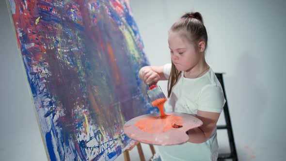 Girl with Special Needs Draws with a Brush on a Large Canvas in a White Room Kid Girl with Down