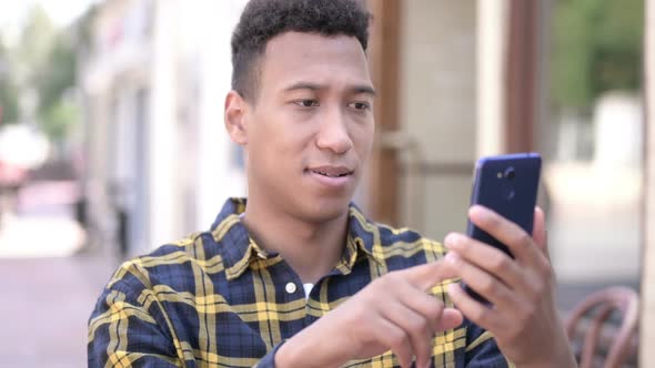 Young African Man Excited for Success on Smartphone Outdoor