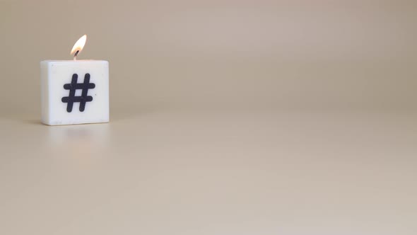 A square candle printed with a hash tag being lit and blown out on a brown background