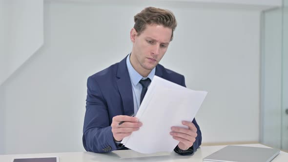 Attractive Young Businessman Reading Documents in Office
