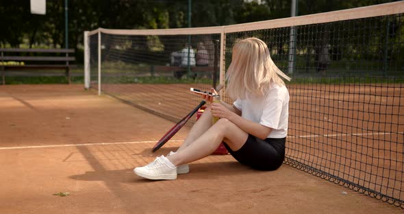 Woman Drinking Water Sitting on Tennis Court