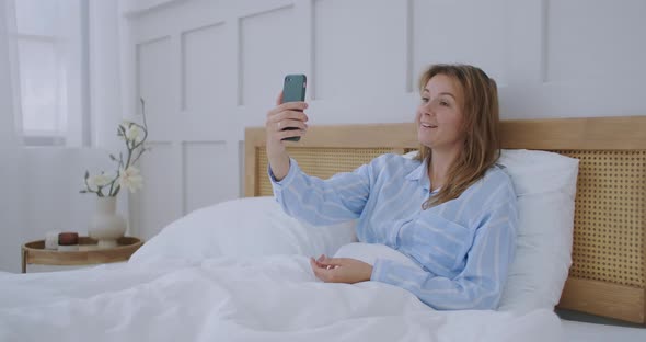 Businesswoman Having a Video Call in Hotel. Happy Girl Lies on the Bed, Talks with Friends Via Video