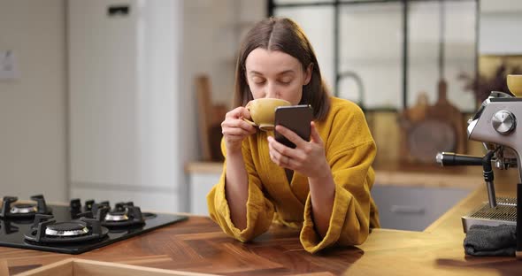 Woman with Coffee and Phone on the Kitchen in the Morning