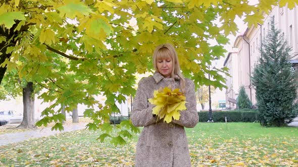 Beautiful Woman with Yellow Leaves Near a Beautiful Tree Rejoices at the Collected Bouquet in the