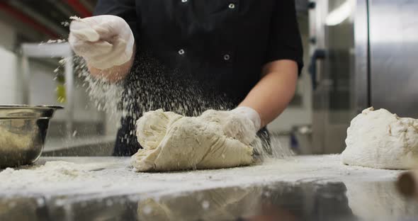 Midsection of caucasian female chef wearing rubber gloves and preparing dough