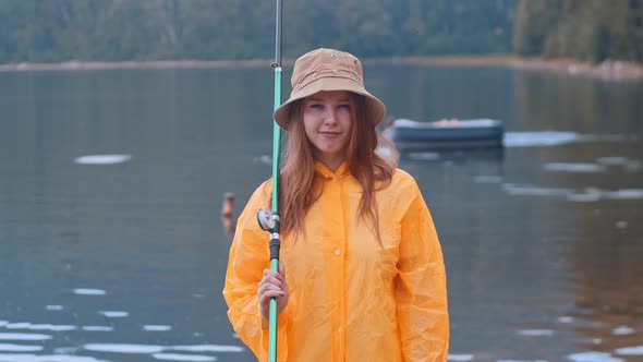 Young Woman in an Orange Raincoat and a Hat on Fishing - Looking in the Camera