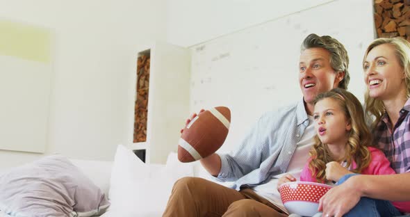 Smiling family watching television while having popcorn in living room 4k