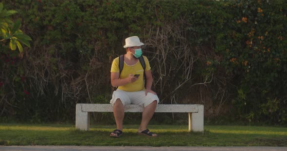 Tourist Man in a Medical Mask Looks for His Way in a Smartphone