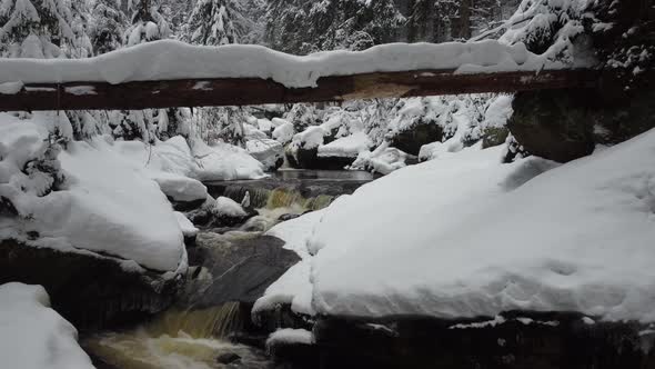 A stream flowing through the winter forest to the waterfall. Aerial view