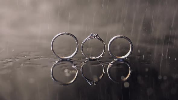 Wedding and Engagement Rings Lying on Dark Water Surface Shining with Light