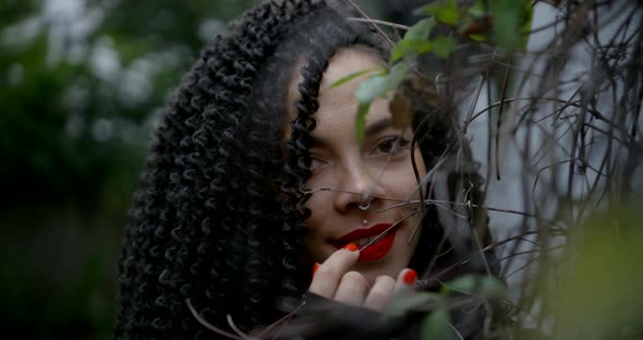 A Close-up Portrait of a Searing Brunette with Curly Hair, Red Lipstick on Her Face, Piercings in