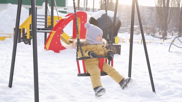 newborn baby in yellow winter clothes swings on a swing