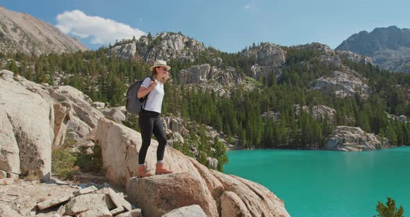 Woman with Arms Raised on Top of Mountain Looking at Scenic Blue Lake View