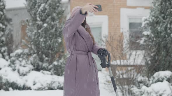 Happy Young Caucasian Woman Taking Selfie Outdoors Standing with Shovel on Snowy Backyard