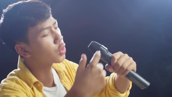 Side View Of Young Asian Boy Holding A Microphone And Rapping On The White Smoke Black Background