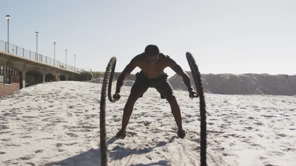 African american man exercising with battling ropes outdoors on the beach