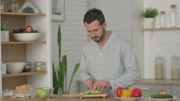 Young Man in Pajamas Peeling Cucumber in Kitchen