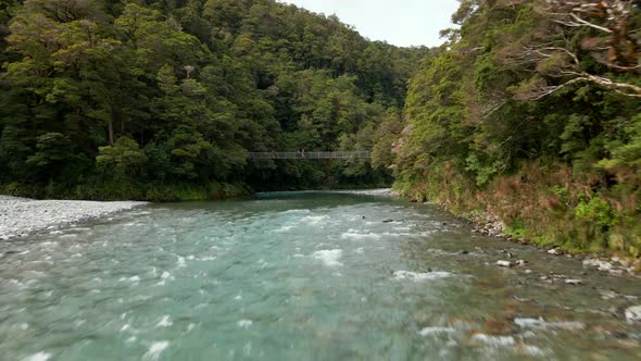 Tourists crossing metal bridge over fast green river in Blue Pools track in New Zealand