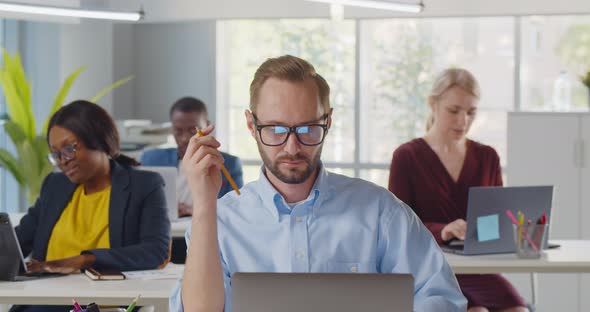 Businessman Sitting at Desk Working on Laptop in Modern Open Plan Office