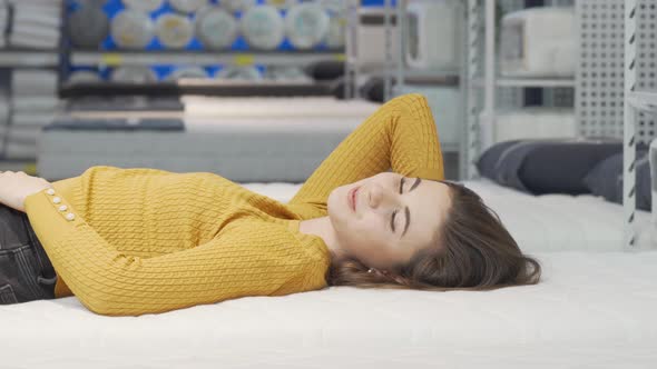 Happy Young Woman Enjoying Lying on New Mattress at Furniture Store