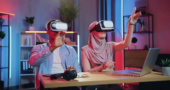 Man and Arabic Woman in Hijab Working on Imaginary Screen in Augmented Reality Goggles in home