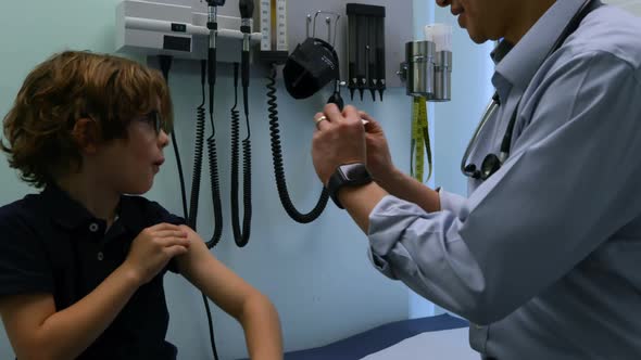 Side view of young asian male doctor applying band aid on caucasian boy patient arm in clinic 4k