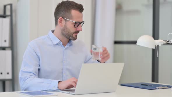 Middle Aged Man Drinking Water While Working on Laptop