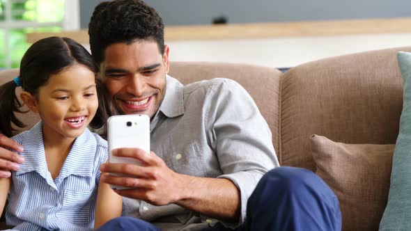 Father and daughter using mobile phone in living room