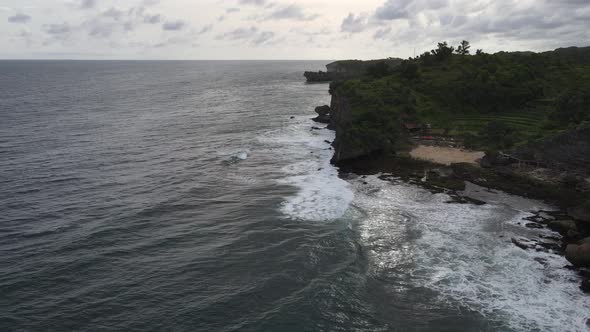 Aerial view of tropical beach in Gunung kidul, Indonesia with green and rocky cliff.