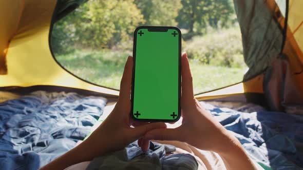 Handheld Firstperson View Woman Holding a Smartphone with a Green Screen While Lying in a Tent