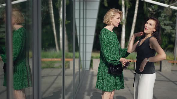 Side View Two Positive Women Talking Gesturing in Slow Motion Standing on Sunny City Street Outdoors