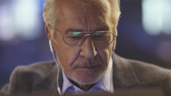 Portrait of an Elderly Grayhaired Man with Glasses Sitting in a Cafe and Looking at a Laptop Screen