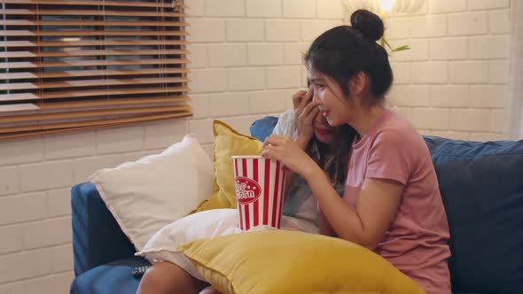 Asian female lover eating popcorn scary and shock while looking horror film together on sofa