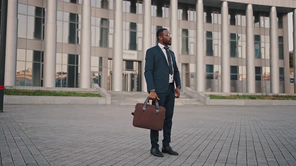 Portrait of Confident African American Businessman Wearing Suit Standing Outdoors with Bag Waiting