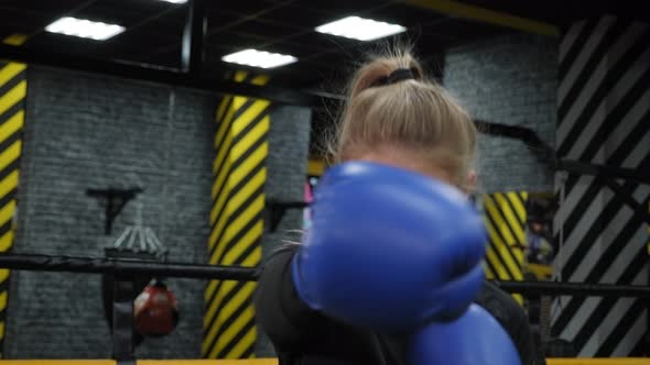 A Young Woman in Blue Boxing Gloves Practices Punches in the Boxing Ring