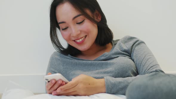 Laughing Asian woman texting by phone