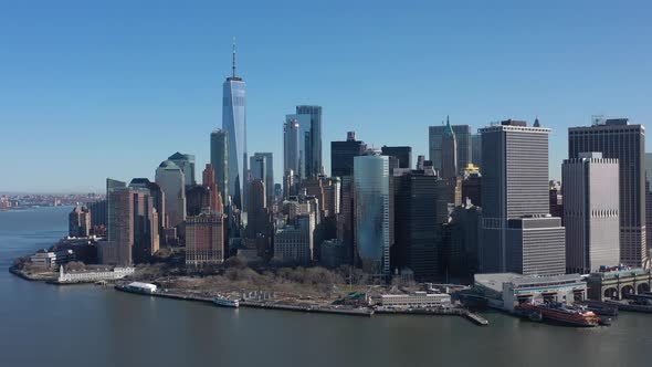 An aerial view of New York Harbor on a sunny day with blue skies. The drone camera facing lower Manh