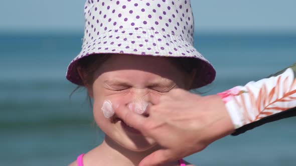 Mother Apply Protective Sunscreen on Daughter Nose at Beach on Summer Vacation
