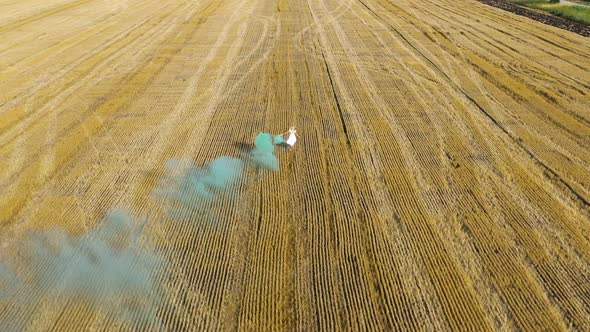 Blond woman in white dress running in a field with green smoke grenade