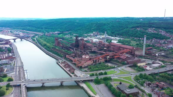 Aerial view of abandoned steel factory with urban background. Next to river and highway with cars dr