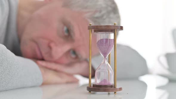 Upset Senior Old Man Looking at Hourglass in Anticipation at Home