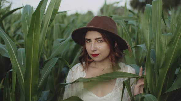 Portrait of Beautiful Young Girl in Hat Standing at a Corn Field Smiling and Looking at Camera with