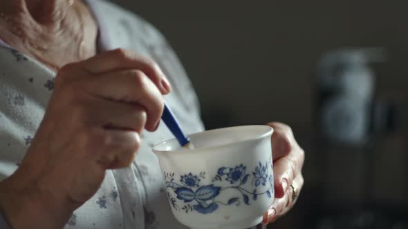 Close Up Of An Old Lady Mixing With A Spoonful In A Cup And Drinking