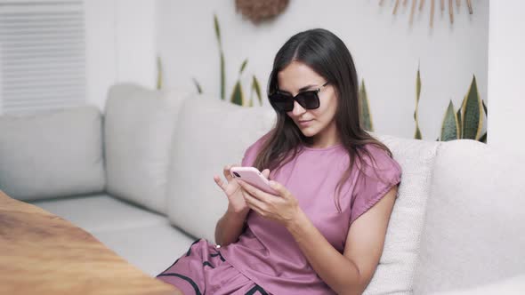 Portrait of Beautiful Woman in Dark Sunglasses Sits in Cafe, Uses Smartphone