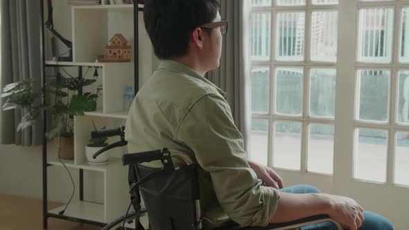 Asian Man Sitting In A Wheelchair Looking Out Of A Door